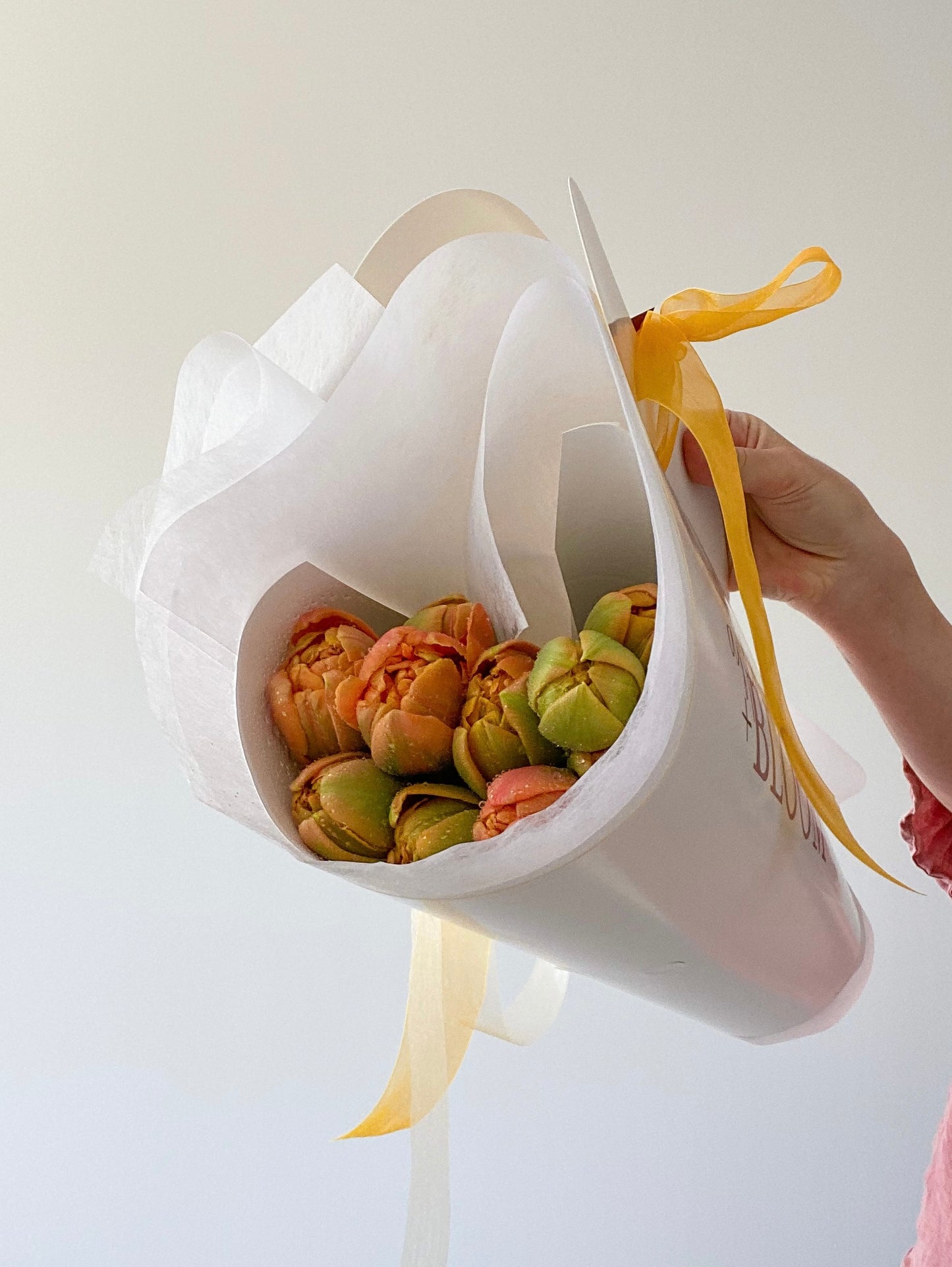 White flower arrangement holder with flowers and a yellow ribbon on a light background