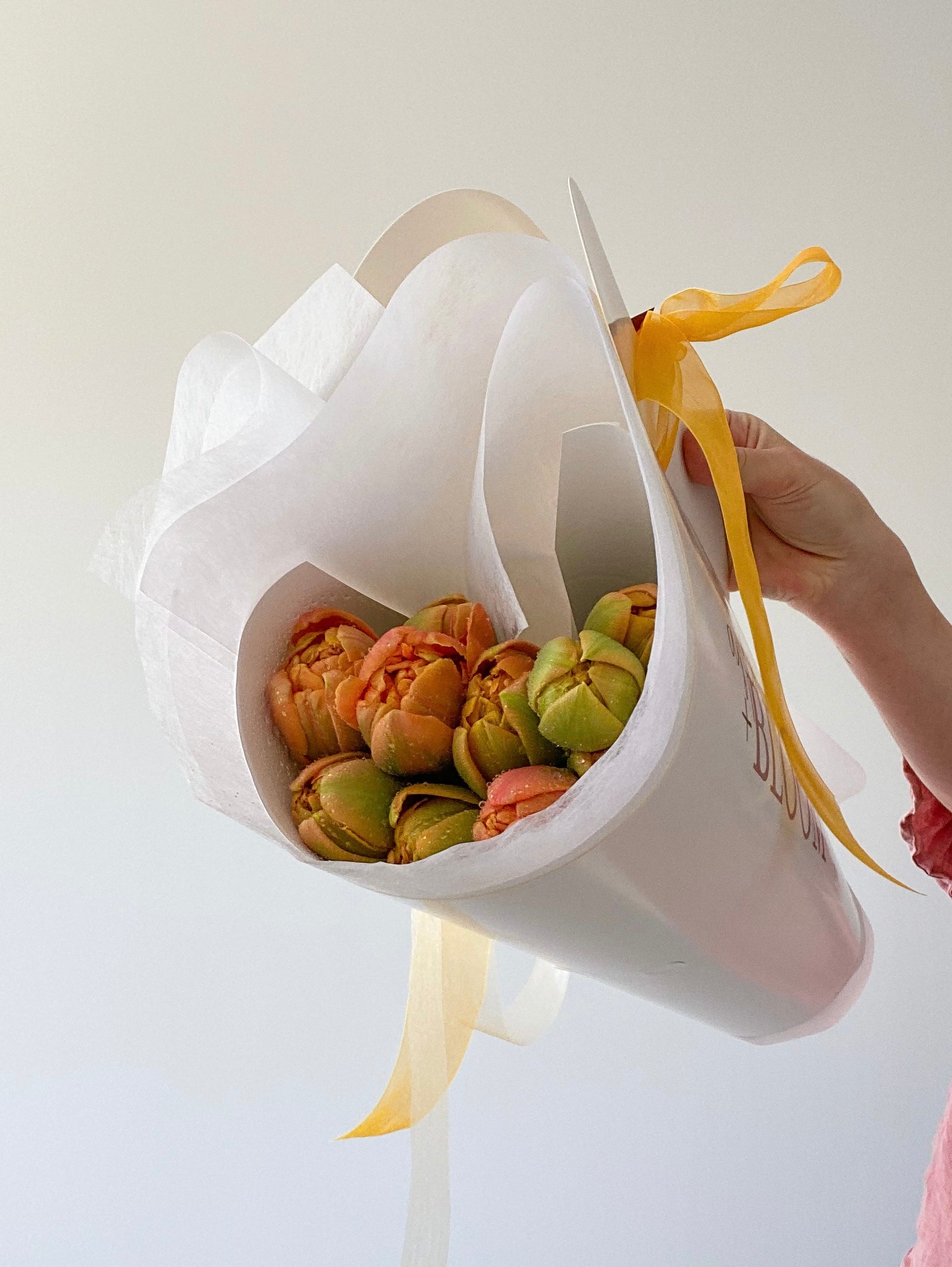 White flower arrangement holder with flowers and a yellow ribbon on a light background